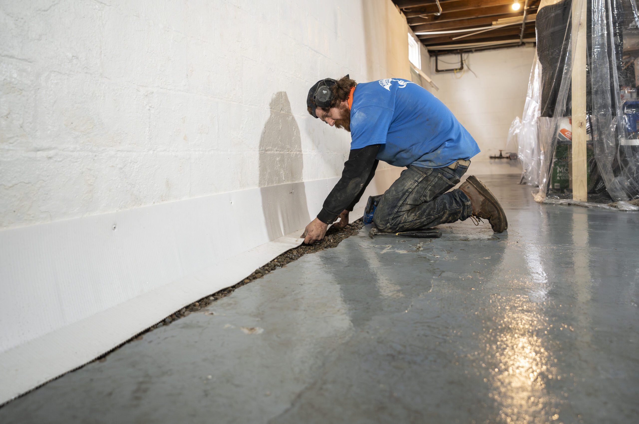 Waterproofing specialist inspecting basement wall seepage with moisture meter and protective equipment