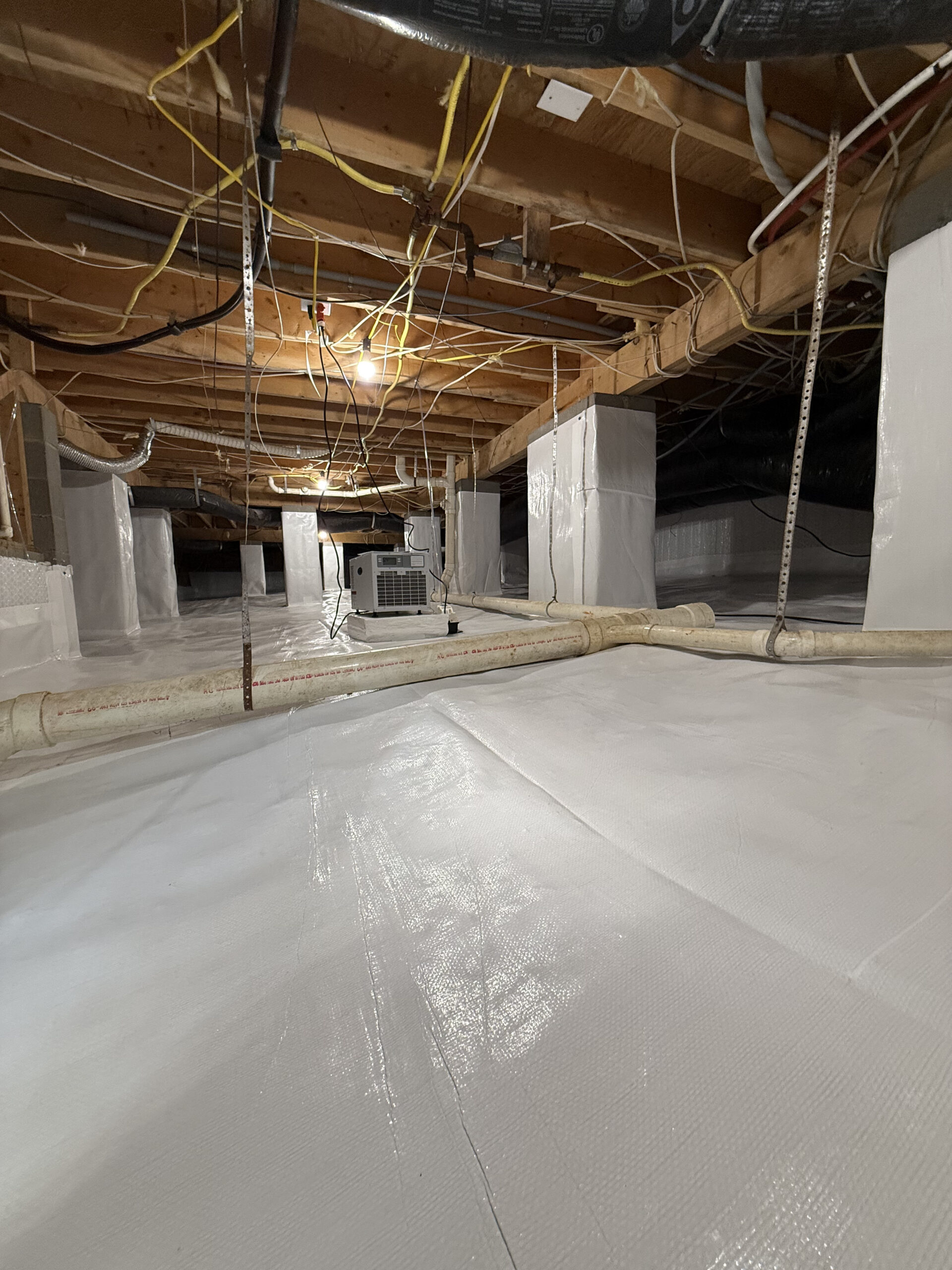 Specialist inspecting crawlspace drainage and moisture barriers with professional lighting and tools