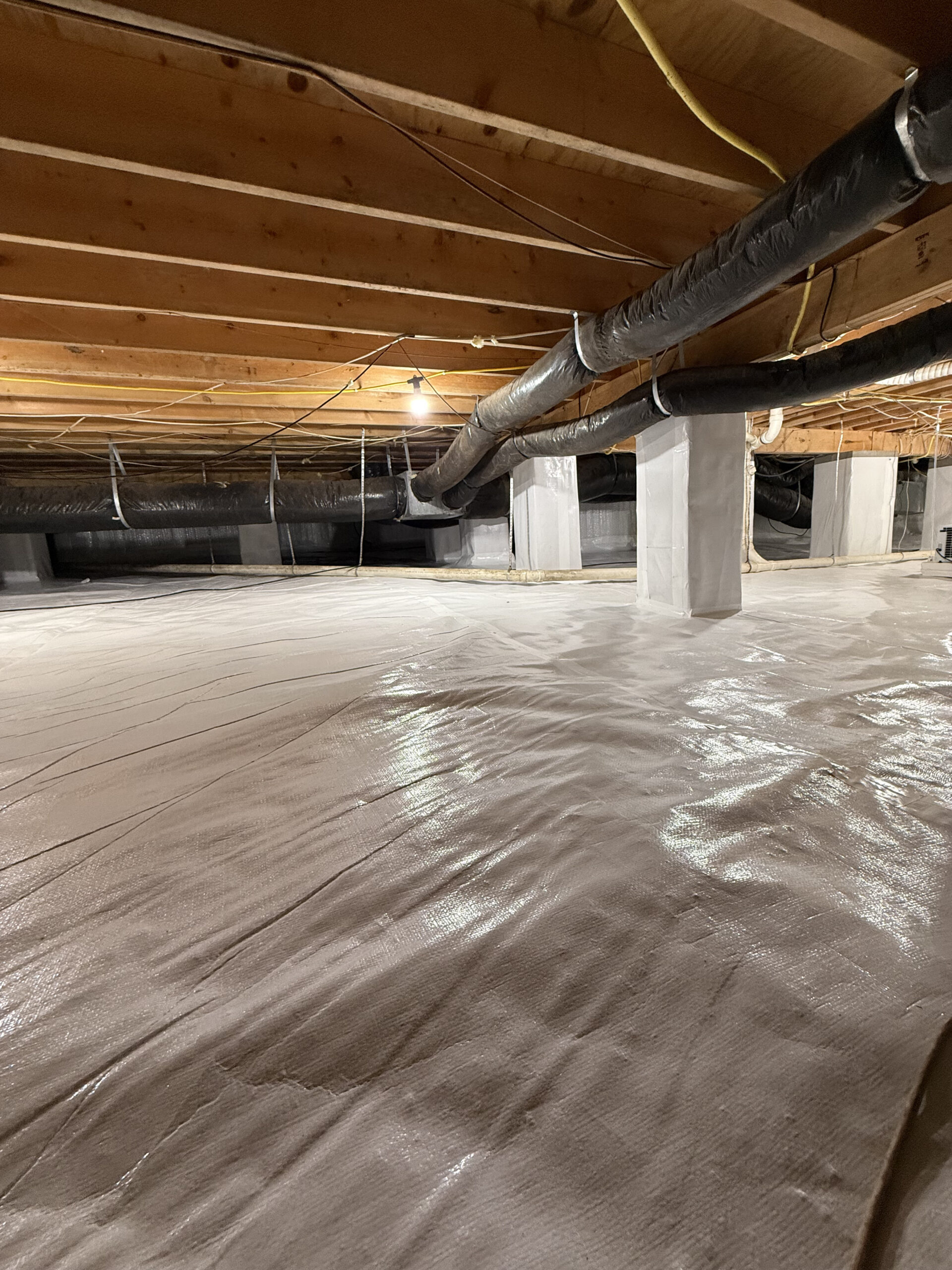 Technician installing vapor barrier in damp crawlspace beneath Central North Carolina home after rainfall