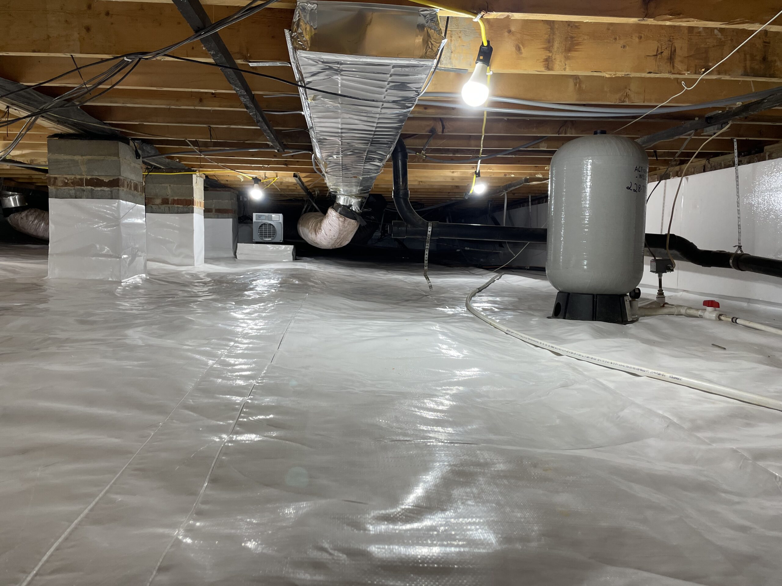 Specialist inspecting crawlspace drainage and moisture barriers with professional lighting and tools